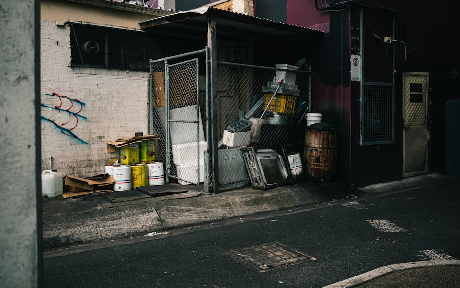 Four black wheeled rubbish bins numbered 33 are lined up along a concrete pavement directly in front of a brick building wall. The wall features a combination of cream and light brown bricks, with thr